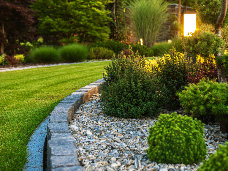 Blick auf einen gepflegten Garten mit Steinen, Gras und verschiedenen Pflanzen.