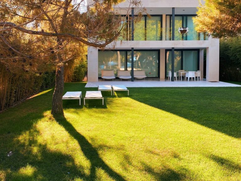 Haus mit großen Fenstern, umgeben von Rasen und Bäumen, im goldenen Licht der Abendsonne.