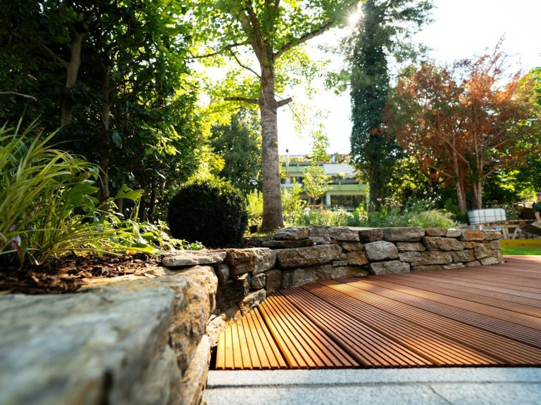 Gartenansicht mit Steinen, Holzterrasse und üppigem Grün.